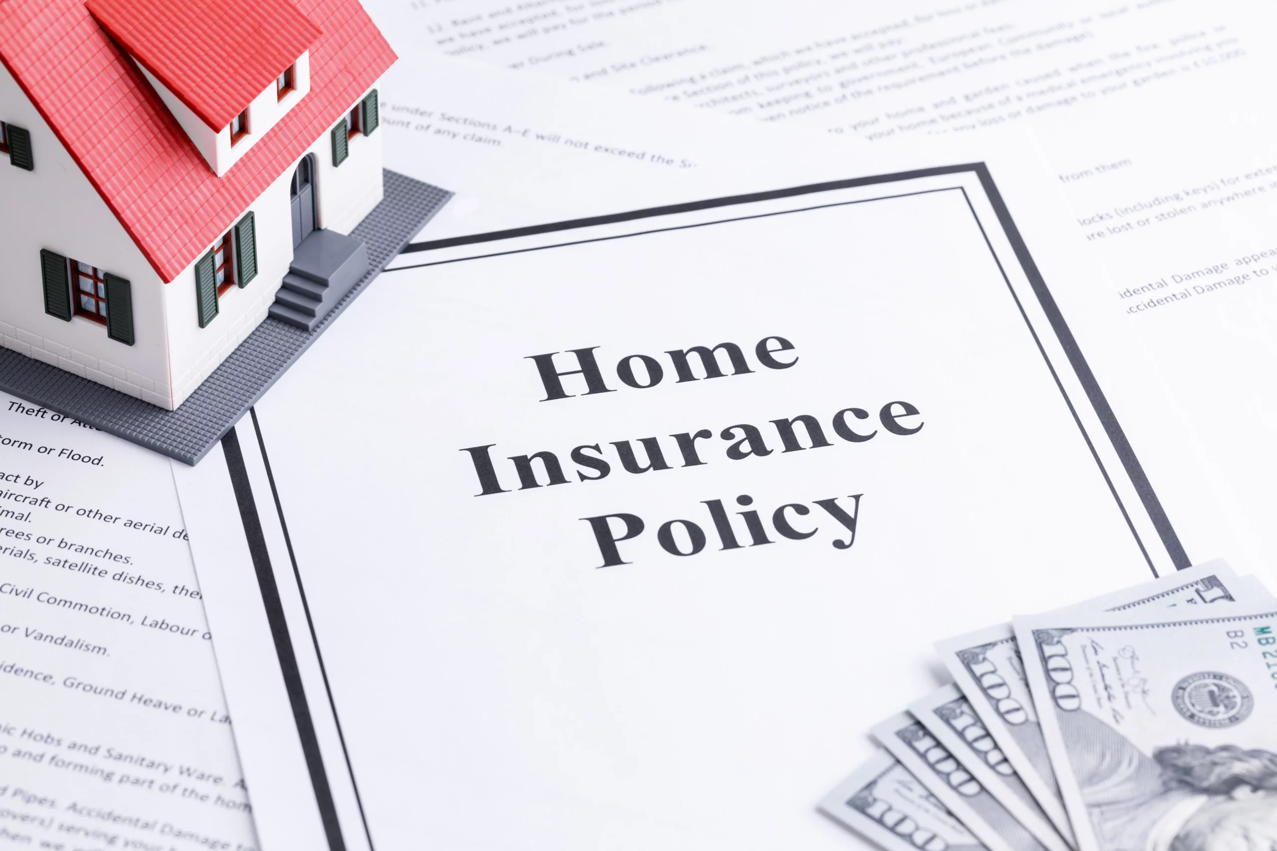 Miniature house and cash on a home insurance policy document, illustrating ways Georgia homeowners can lower home insurance premiums while maintaining reliable property coverage.